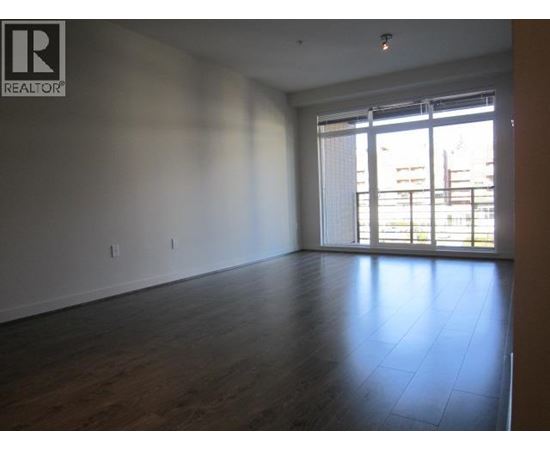 A large empty room with wooden floors and a window with blinds.