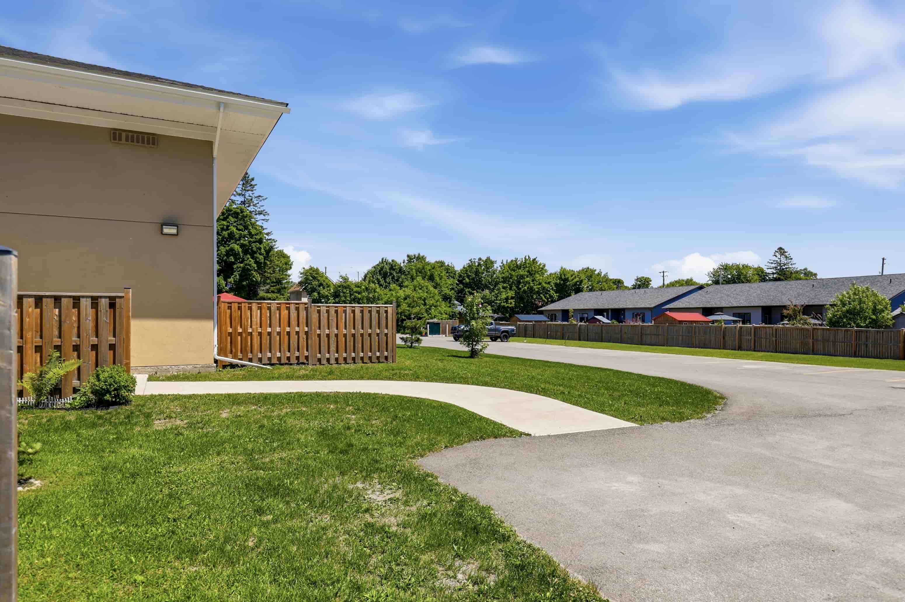 A building with a brown fence and a sign that says "Bank of the West" is surrounded by a grassy area and a paved walkway.