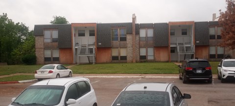 A white car is parked in front of a building with a black car behind it.