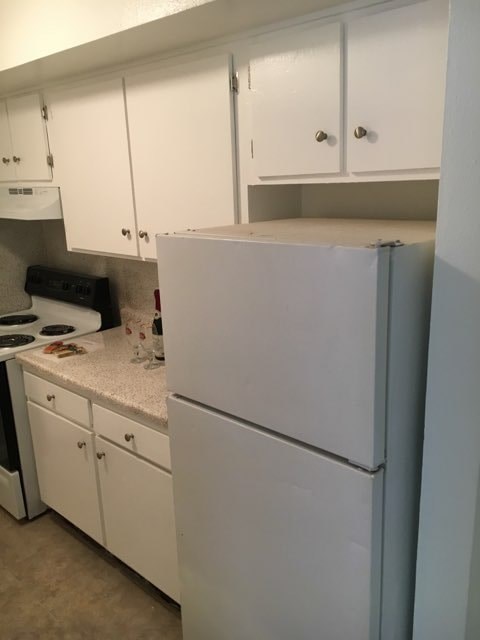 A white refrigerator in a kitchen with white cabinets.