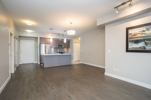A spacious living room with a kitchen in the background and a painting on the wall.