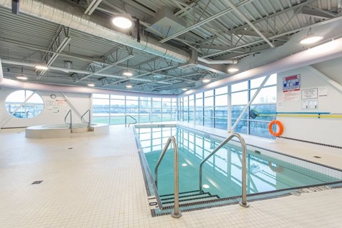 A large indoor swimming pool with a diving board and safety railings.
