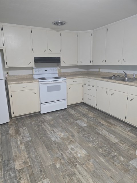A kitchen with white cabinets and a wood floor.
