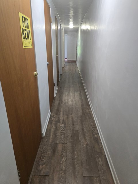 A long hallway with a yellow sign on the door that says "For Rent".