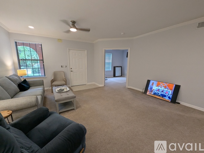 A living room with a grey couch, a grey armchair, a grey ottoman, a flat screen TV and a ceiling fan.
