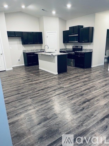 A modern kitchen with black cabinets and a wooden floor.