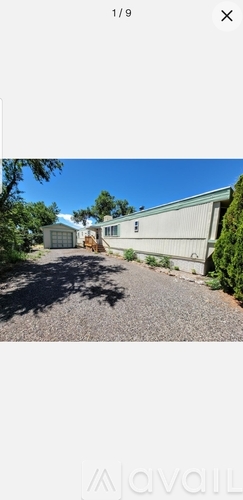 A gravel driveway leads to a white building with a metal roof.