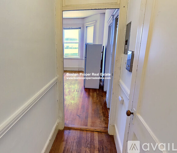 A hallway with a wooden floor and white walls leading to a door.