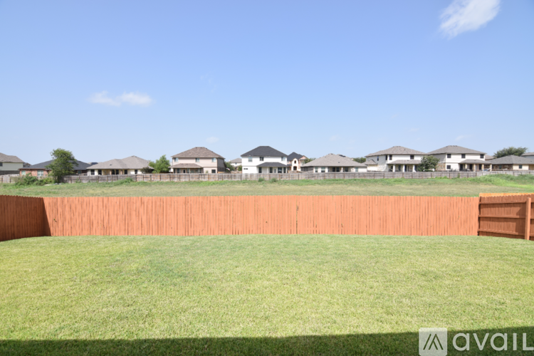 A grassy field with a fence and houses in the background.