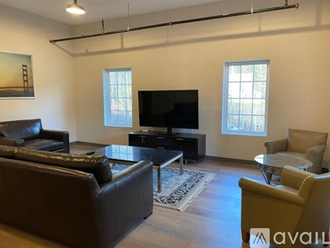 A living room with a black leather couch, a coffee table, a television, and a rug.