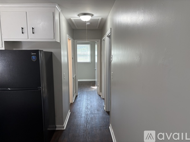A long hallway with a black fridge on the left and a light on the ceiling.
