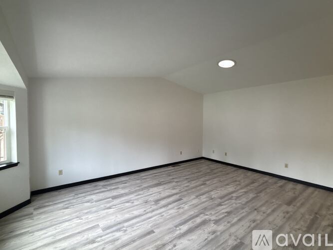 A spacious room with wooden flooring and a window on the left side.