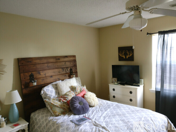 A bedroom with a bed, nightstand, and a television on the wall.