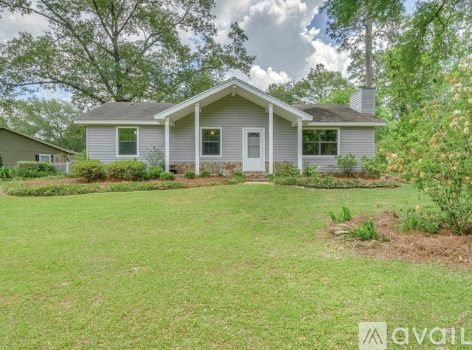 A house with a grey roof and white trim is surrounded by a green lawn and trees.