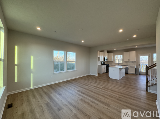 A spacious living room with wooden flooring and a staircase on the right side.