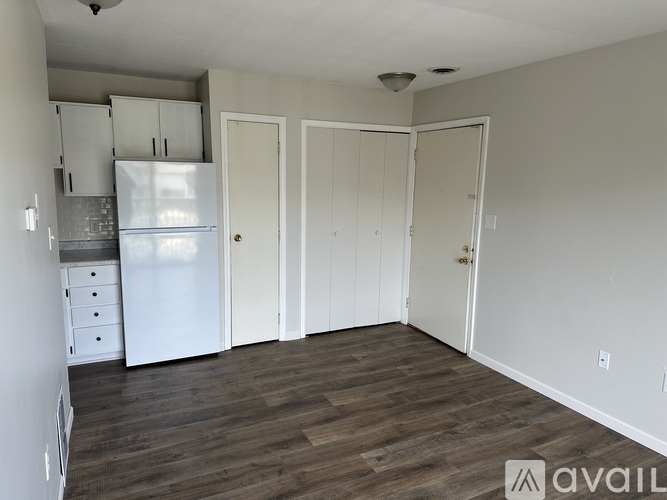A kitchen with a refrigerator, cabinets, and a wooden floor.