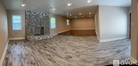 A spacious living room with a stone fireplace and wood flooring.