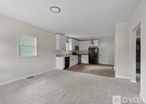 A spacious kitchen and living room with white walls and a grey carpet.