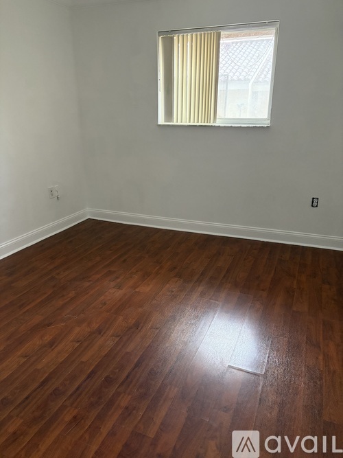 A room with wooden flooring and a window with yellow curtains.