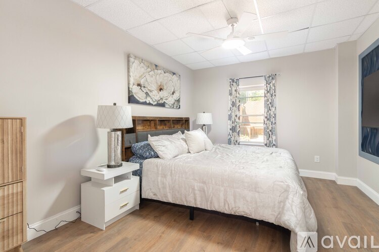 A bedroom with a large bed, a nightstand with a lamp, and a painting on the wall.