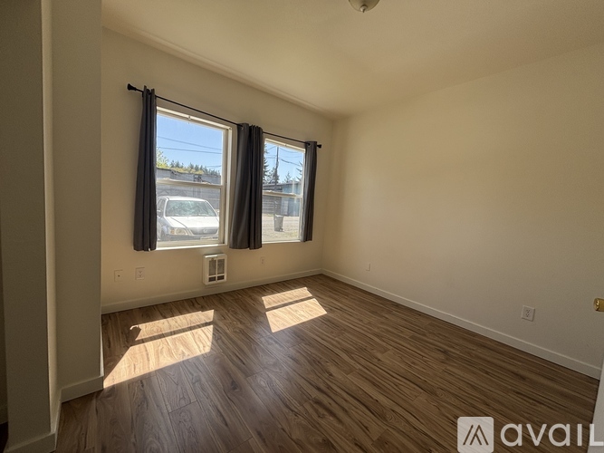 A room with wooden flooring and a window with a view of a car and trees outside.