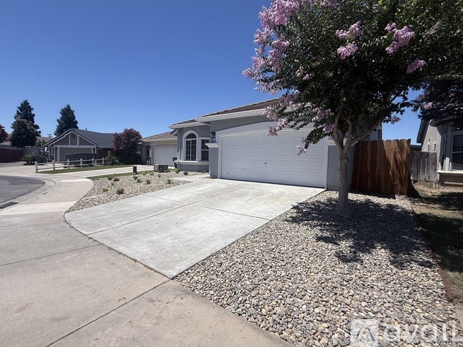 A house with a white garage door and a tree with pink flowers in front.