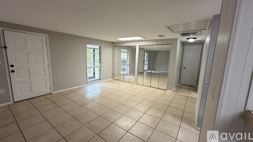 A spacious room with tiled flooring and white walls, featuring a door, a window, and a mirror.