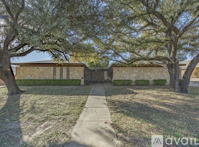 A house with a stone wall and a tree in front.