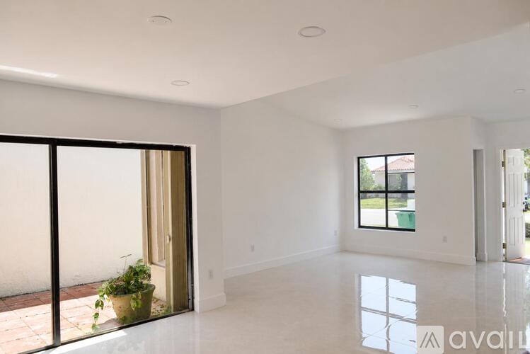 A large, empty room with a sliding glass door and a potted plant on the patio outside.