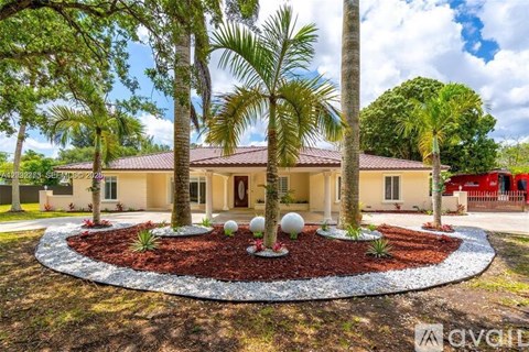 A house with a red roof and a garden with a circular bed of red mulch and white spherical decorations in front of it.