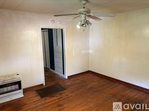 A room with a ceiling fan and a brown rug on the wooden floor.