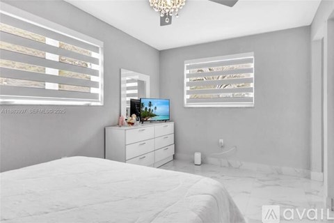 A bedroom with a large bed, a dresser with a television, and a chandelier.
