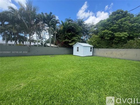 A small white house is situated in a grassy backyard with a fence and trees in the background.
