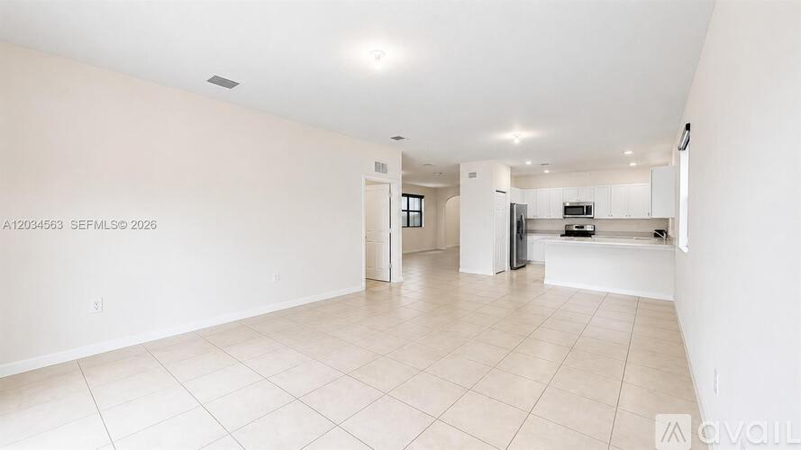 A spacious, empty living room with white walls and flooring.