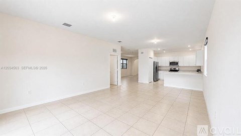 A spacious, empty living room with white walls and flooring.