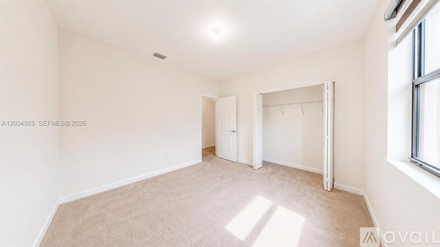 A spacious room with a carpeted floor and a window on the right side.