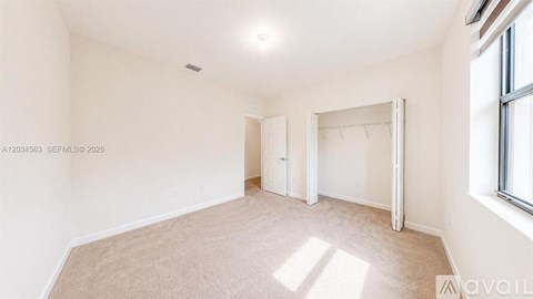 A spacious room with a carpeted floor and a window on the right side.