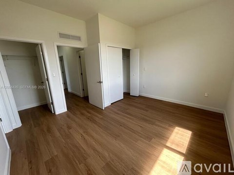 A room with wooden flooring and white walls, with a door on the left and another on the right.