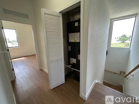 A room with a white door and a window with a view of trees outside.