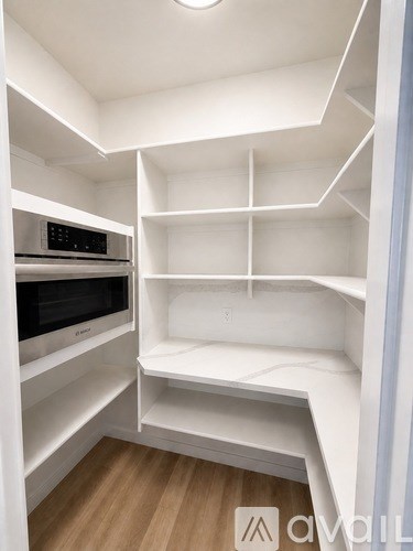 A white kitchen pantry with a microwave and shelves.