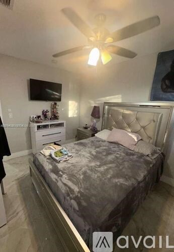 A bedroom with a bed, a ceiling fan, and a TV mounted on the wall.