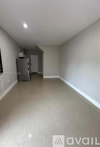 A spacious empty room with a refrigerator in the corner.