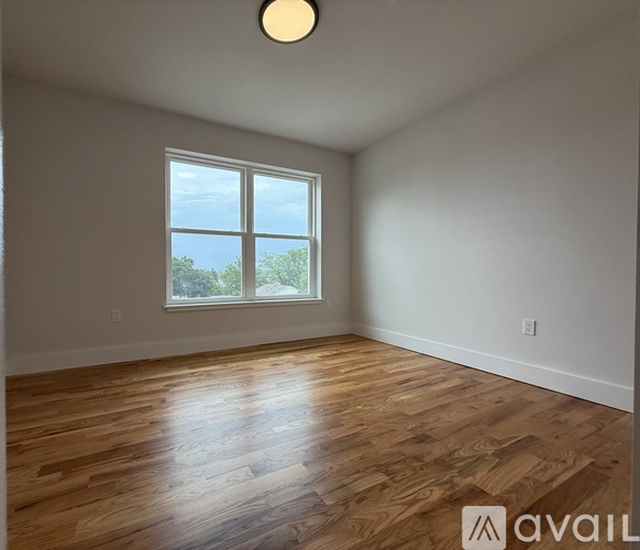 A room with wooden flooring and a window overlooking trees.