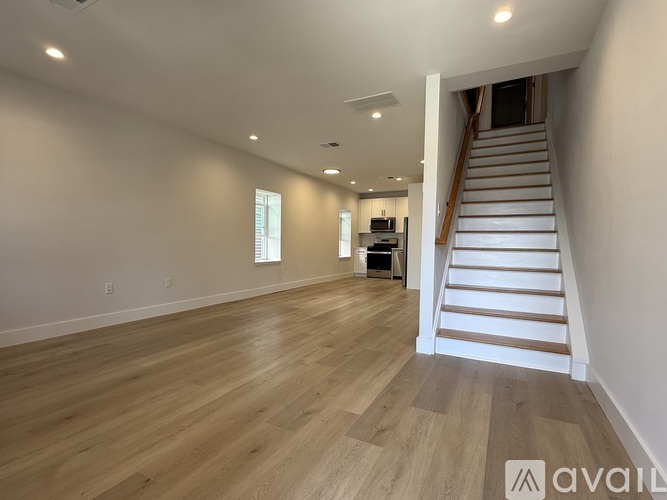 A spacious room with wooden flooring and a staircase leading to another level.