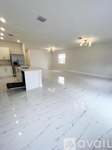A spacious room with marble flooring and a kitchen area.