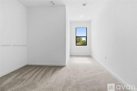 A room with a carpeted floor and a window showing a view of trees.