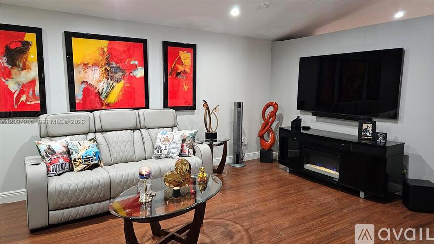 A living room with a grey couch, a glass coffee table, a television, and three paintings on the wall.