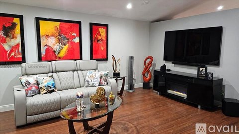 A living room with a grey couch, a glass coffee table, a television, and three paintings on the wall.