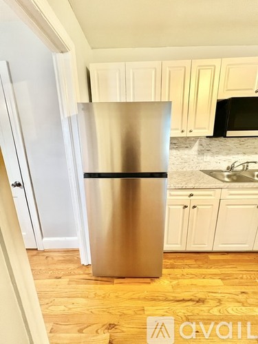 A stainless steel refrigerator in a kitchen with wooden floors.