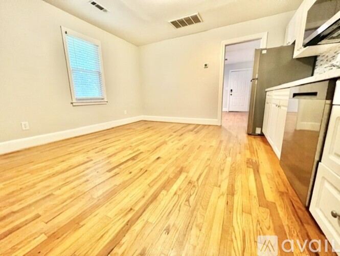 A kitchen area with wooden flooring and a window with blinds.